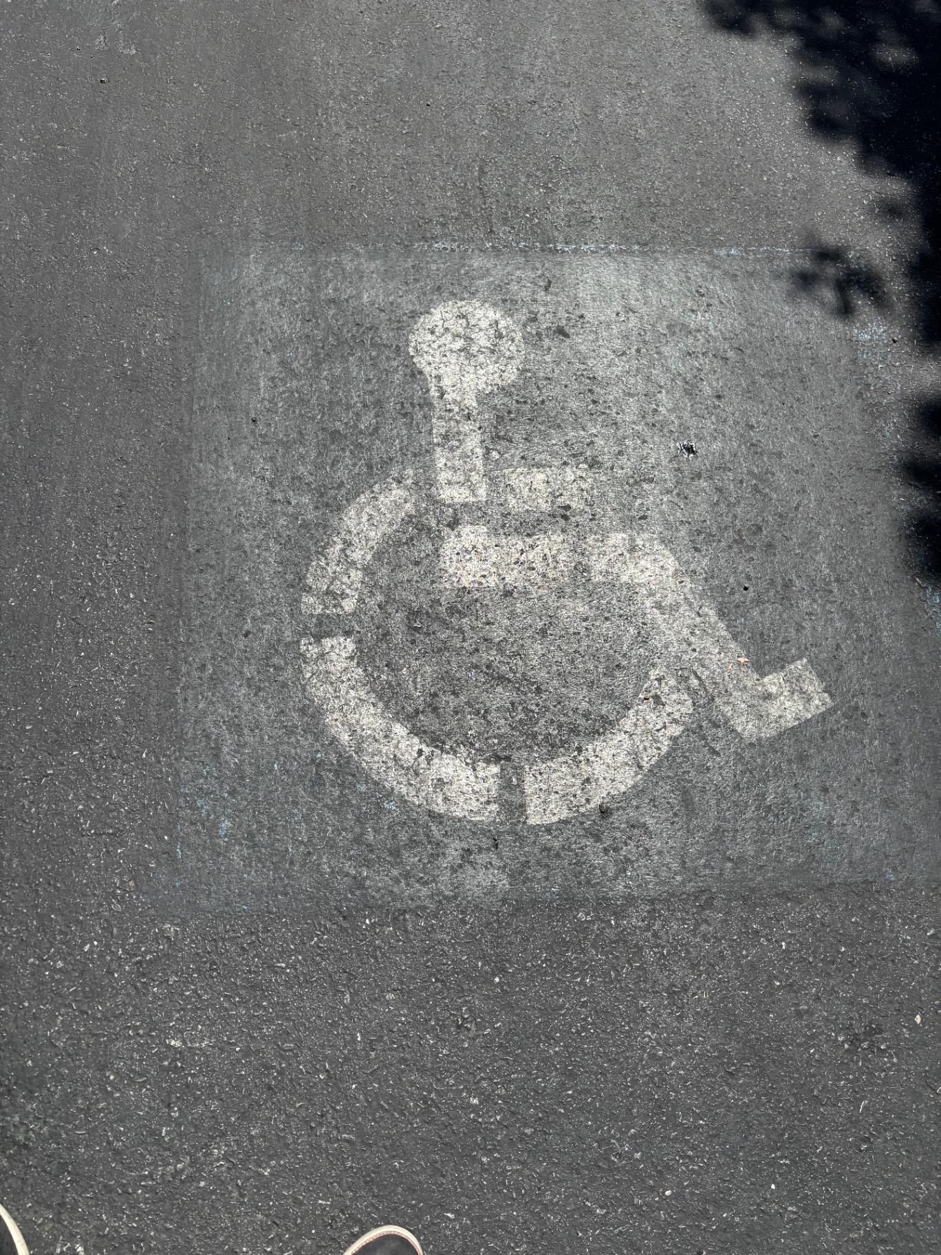 Worn white accessibility symbol painted on dark asphalt